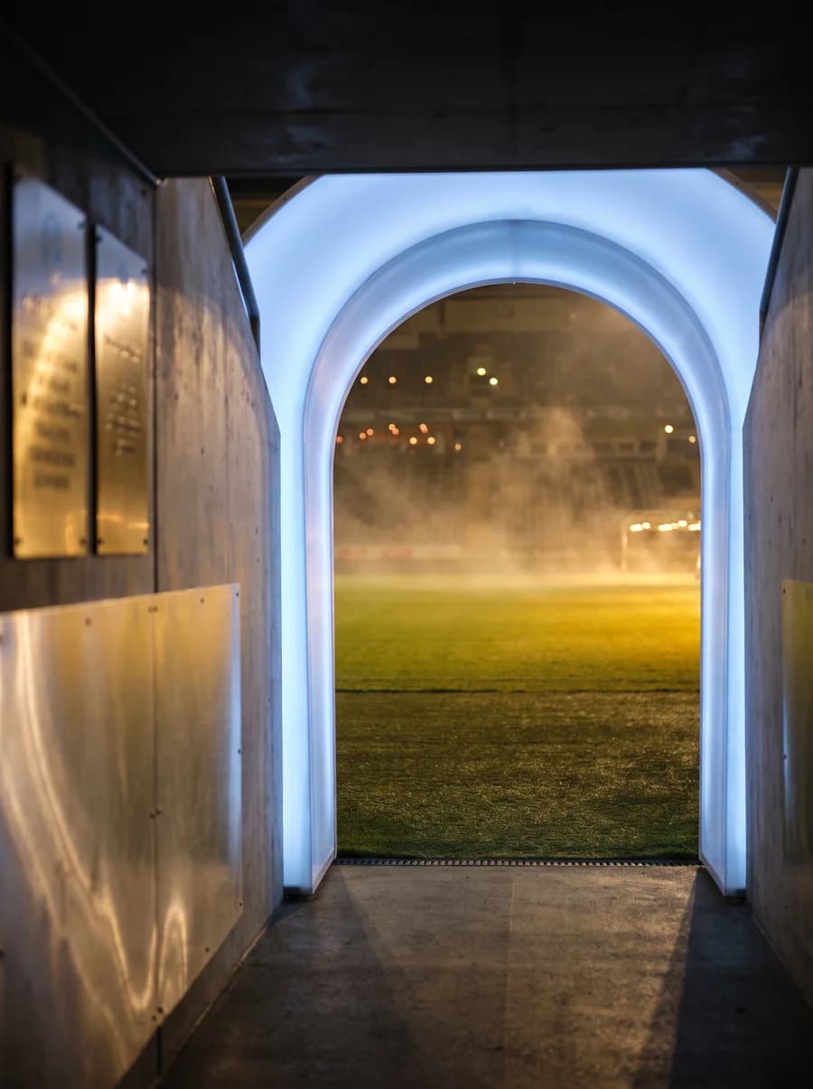 Floodlit stadium tunnel opening onto misty green turf